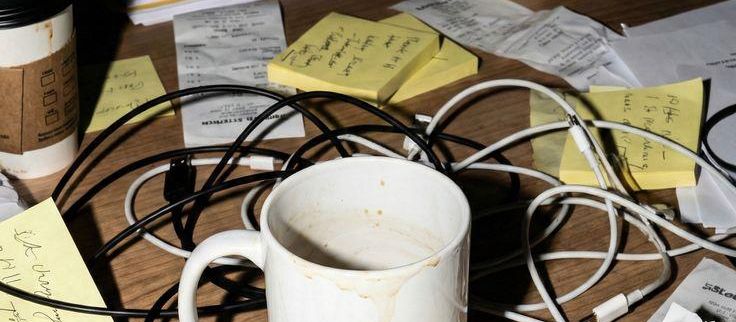 A desk covered in sticky notes, tangled cables and a cold coffee