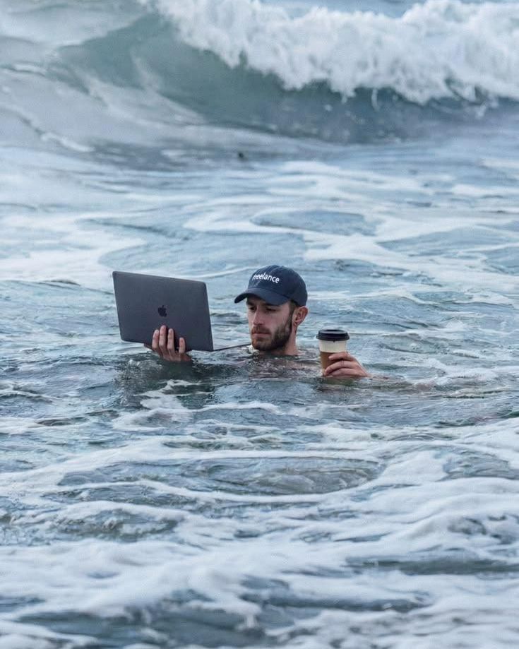 Alguien trabajando con el portátil metido en el mar, con un café en la mano